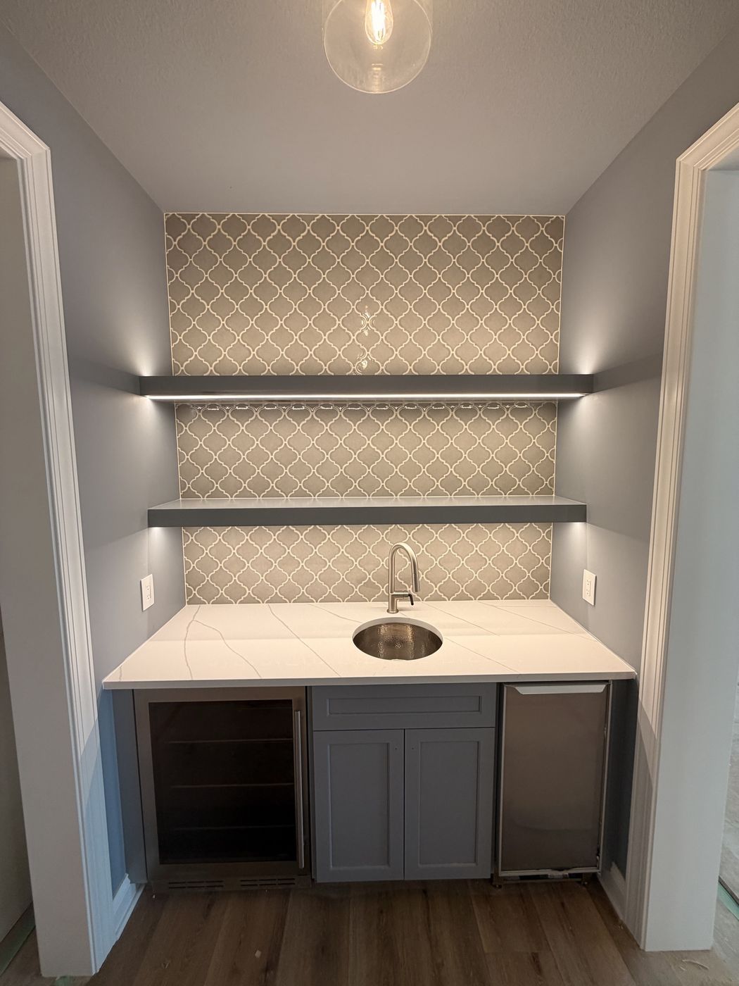 Wet bar with an arabesque tile backsplash and floating shelves