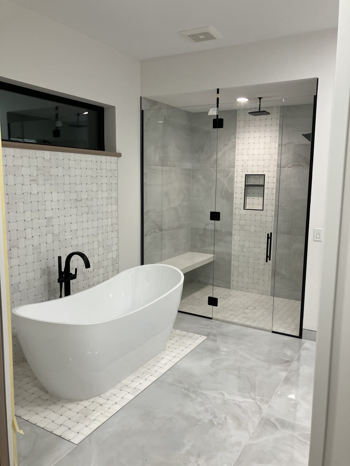 Master bathroom with a freestanding tub on a basketweave mosaic and a glass-enclosed shower with large-format tile