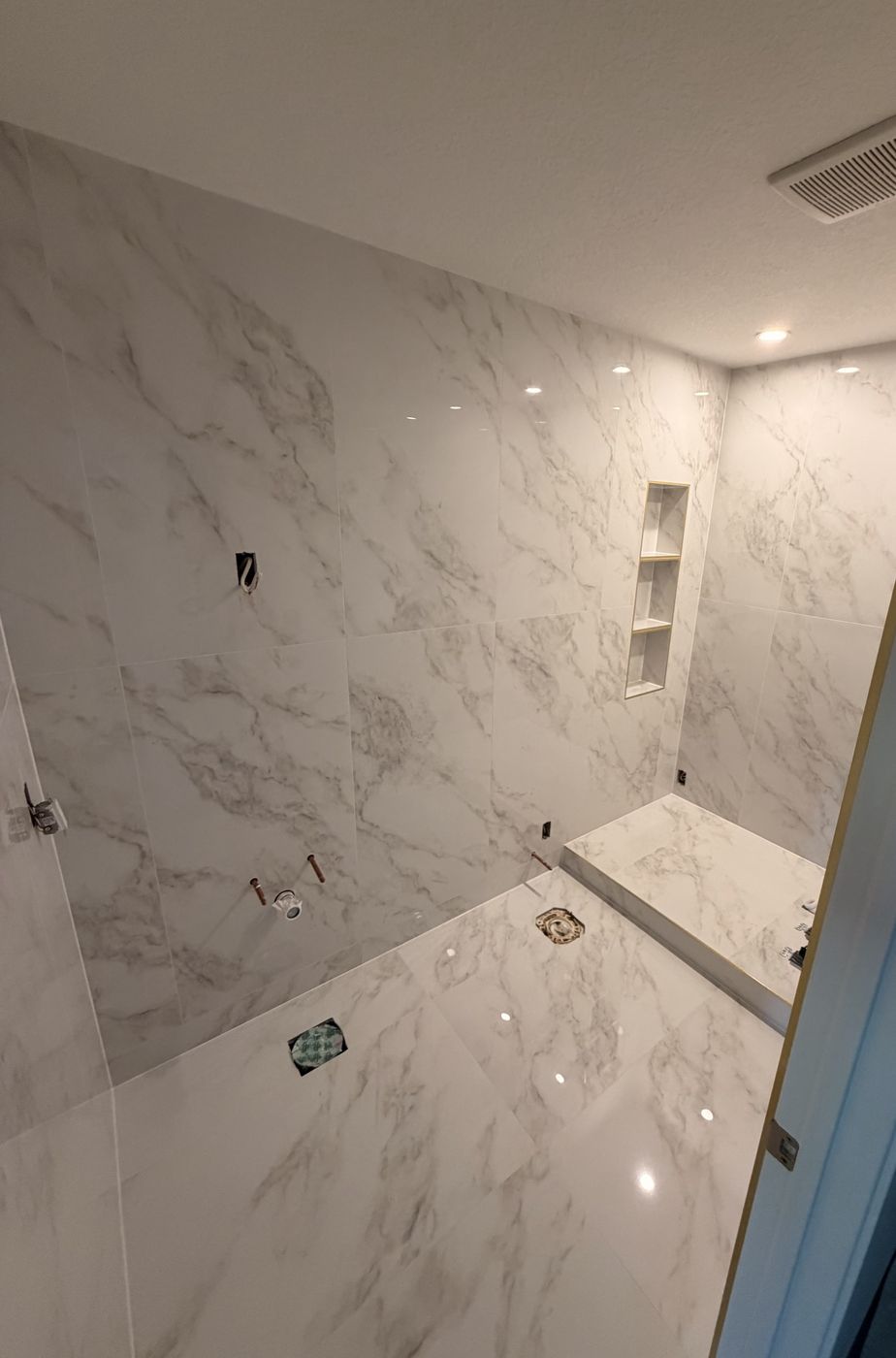 Large-format marble-look tile shower with a recessed niche and curb